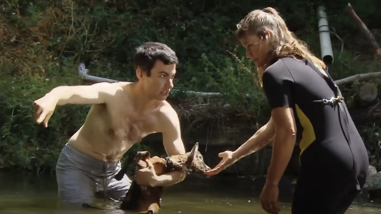 Nathan Fielder shirtless in a pond holding a baby goat with a zookeeper in Nathan For You