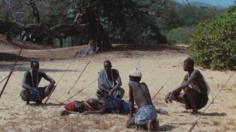 Diola villagers standing around a fallen man in a spear-covered field in Emitaï
