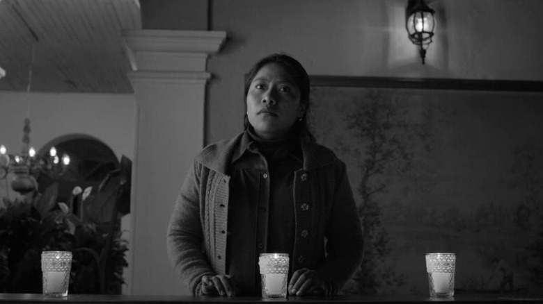 Yalitza Aparicio as Cleo Gutiérrez standing in a balcony lined with candles in Roma
