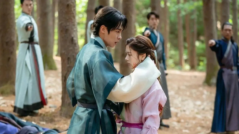Jang Uk (Lee Jae-wook) holds a bloody Mu-deok (Jung So-min) surrounded by mages in Alchemy of Souls