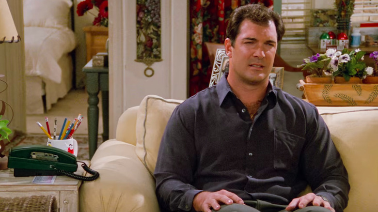 Patrick Warburton as David Puddy sits on a couch in Seinfeld