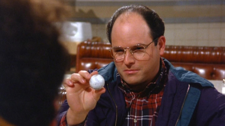 George (Jason Alexander) holds up a golf ball in Seinfeld