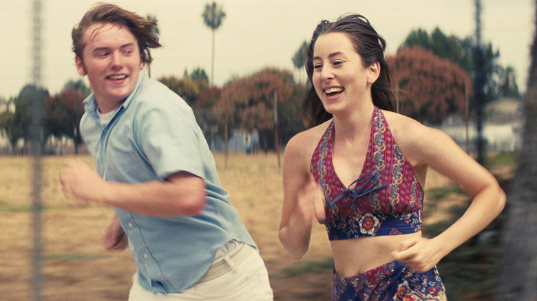 Cooper Hoffman as Gary running with Alana Haim as Alana in Licorice Pizza