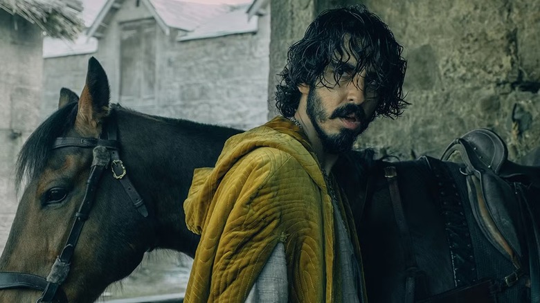 Wet Sir Gawan (Dev Patel) stands by his horse.