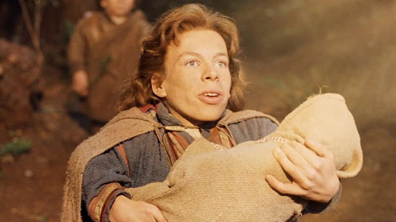 Warwick Davis as Willow holding a baby as light glows upon them