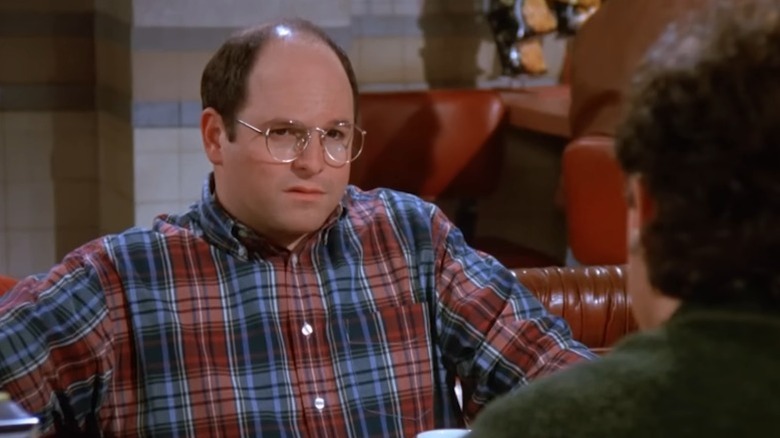 Jason Alexander as George Constanza sitting at a diner table on Seinfeld