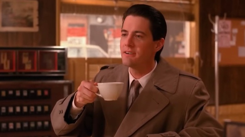 Kyle MacLachlan as Special Agent Dale Cooper holding a cup of coffee and smiling on Twin Peaks