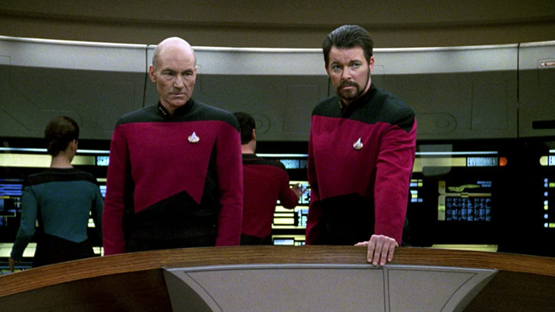 Patrick Stewart as Jean-Luc Picard stands next to Jonathan Frakes as Will Riker on the Enterprise bridge in Star Trek: The Next Generation.