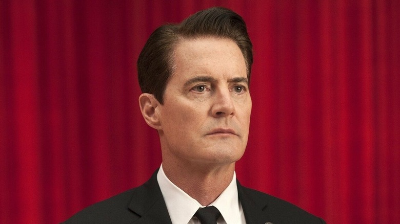 Kyle Maclachlan as Dale Cooper, sitting in front of a red curtain on Twin Peaks