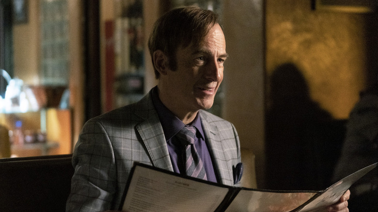 Bob Odenkirk as Saul Goodman smiles while reading a menu in Better Call Saul.