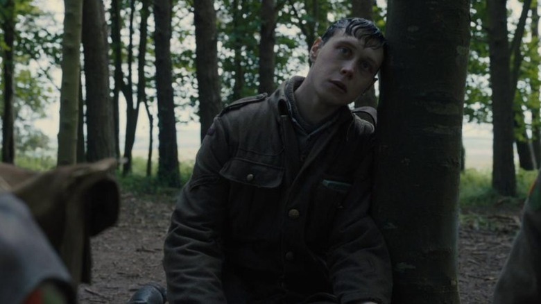 George MacKay as Lance Corporal Schofield sitting on the ground and resting his head against a tree in 1917