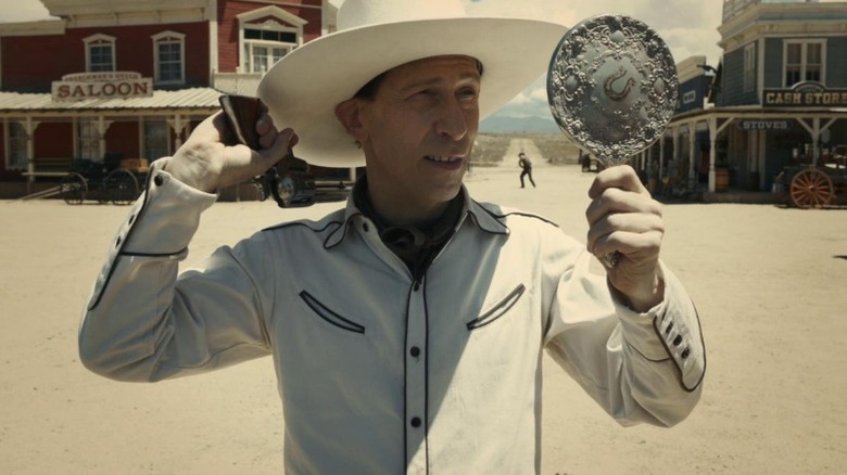Tim Blake Nelson as Buster Scruggs using a hand mirror to point a gun at a man behind him in The Ballad of Buster Scruggs
