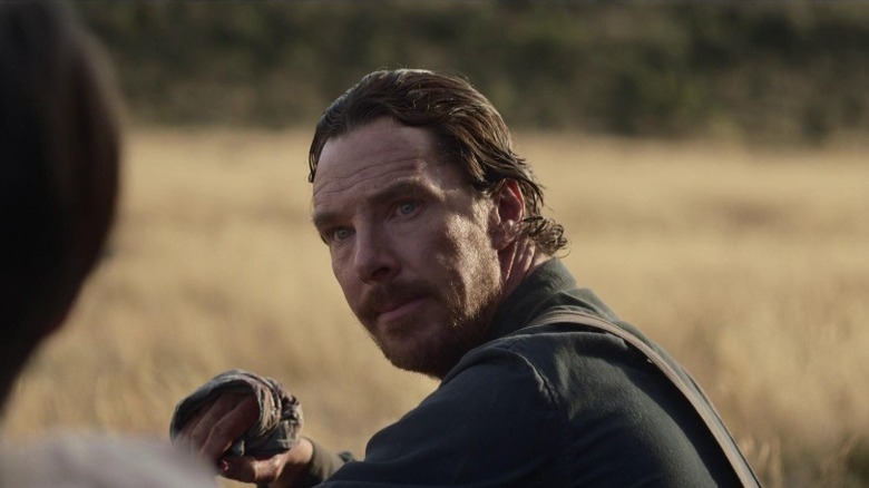 Benedict Cumberbatch as Phil Burbank sitting on a field and looking at Kodi Smit-McPhee as Peter Gordon in The Power of the Dog