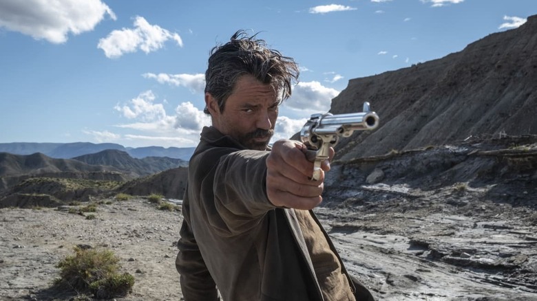 Arthur McCoy (Dominic Cooper) aims a revolver in That Dirty Black Bag