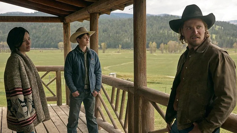 Kayce Dutton (Luke Grimes) stands on a porch with Monica (Kelsey Asbille) and Tate (Brecken Merrill) in Yellowstone