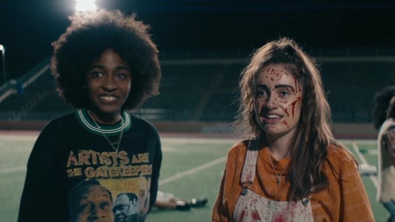 Ayo Edebiri as Josie standing next to Rachel Sennott as PJ covered in blood on a football field in Bottoms