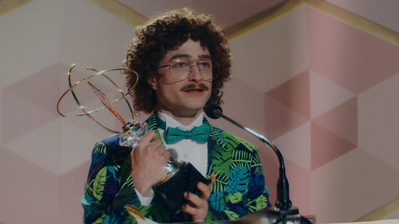 Daniel Radcliffe as Weird Al with an afro and mustache in a tropical suit holding an award in Weird the Al Yankovic Story