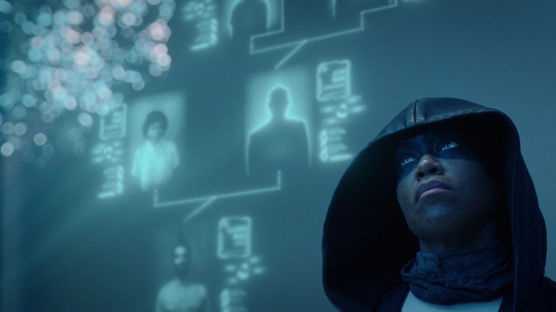 Regina King as Angela Abar wearing hood and black face paint standing in front of blue screen in Watchmen
