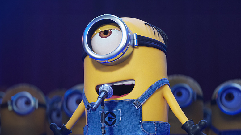 Mel (Pierre Coffin) speaks into a microphone surrounded by other Minions in Despicable Me 3