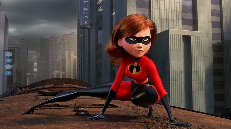 A glaring Elastigirl (Holly Hunter) kneels on top of a train speeding through a city in Incredibles 2