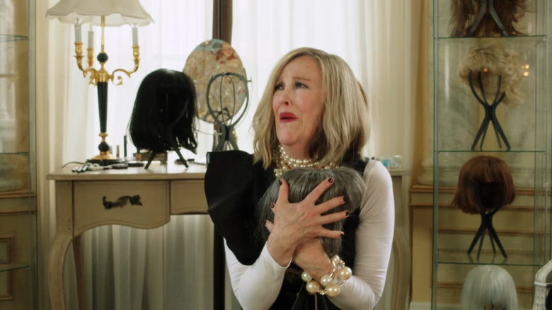 Moira clutches a wig in her arms, crying 