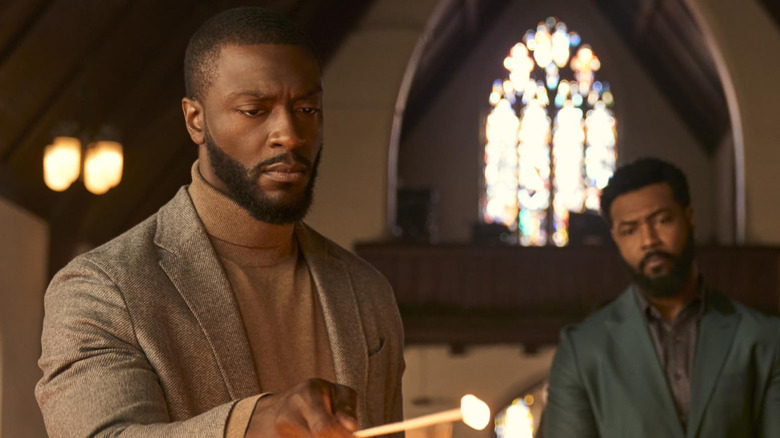 Aldis Hodge as Alex Cross lights a candle while Isaiah Mustafa as John Sampson looks on in Cross