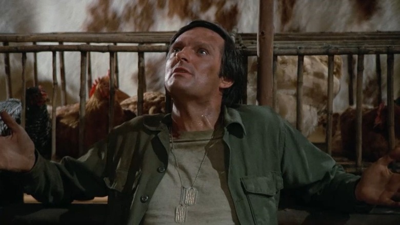 Alan Alda as Hawkeye Pierce sitting in front of a crate of chickens in M*A*S*H