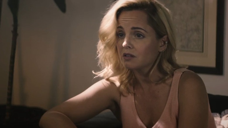 Mena Suvari as Nicole Brown Simpson sitting on a couch and speaking with her brows raised in The Murder of Nicole Brown Simpson