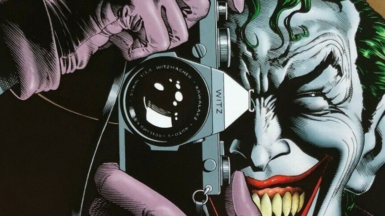 The Joker smiles while holding a camera up to his eye