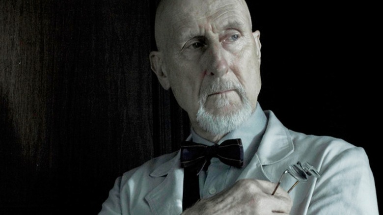 Dr. Arden looks off to the side, holding his glasses