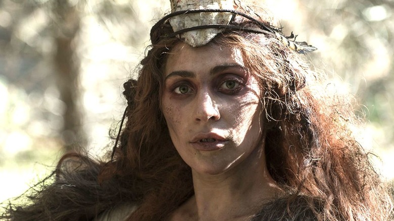 A woman, with wild hair and a dirty face, looks at the camera