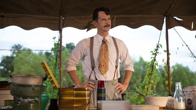 Stanley stands with his hands on his hips in front of a table
