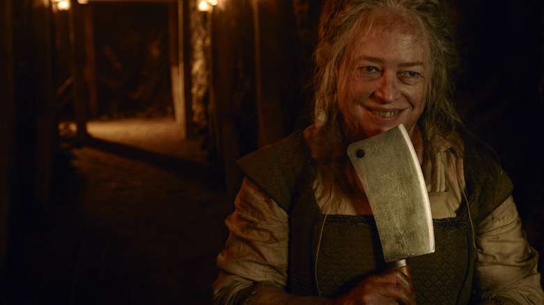 A woman grins threateningly, holding up a meat cleaver