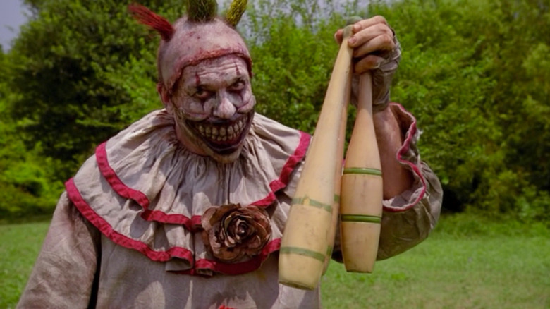 A terrifying wide-mouthed clown holds up two pins