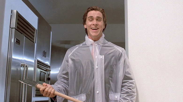 Patrick Bateman wears suit covered in a poncho and holds axe in American Psycho