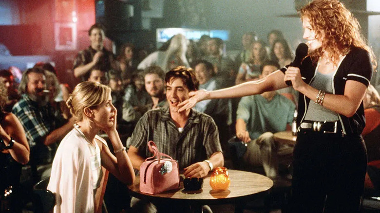 Julianne points at Kimmy at a karaoke bar with Michael cheering her on.