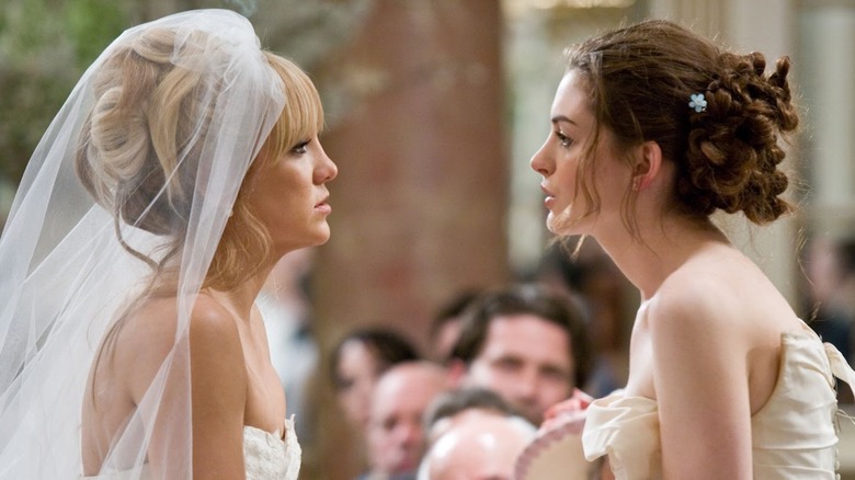 Olivia Lerner and Emma Allan staring at each other in bridal gowns.