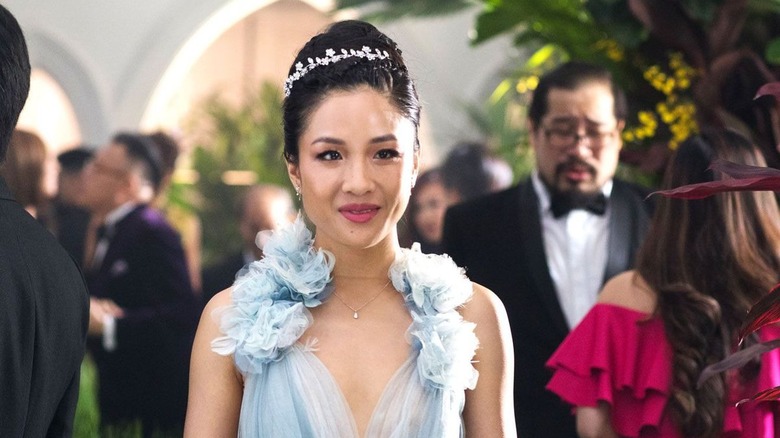 Rachel Chu smiles at a wedding in a blue evening gown.
