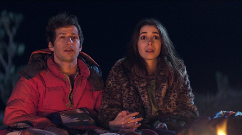 Nyles and Sarah staring hopefully next to a campfire holding hands.
