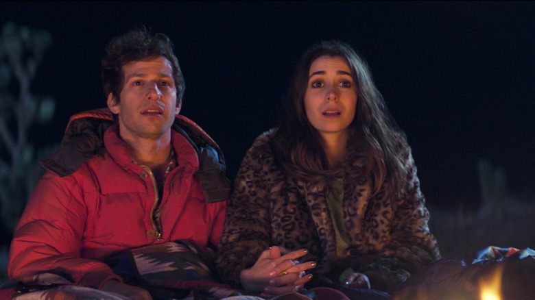 Nyles and Sarah staring hopefully next to a campfire holding hands.
