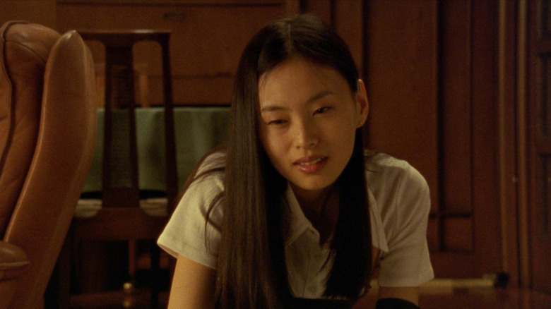 Eihi Shiina as Asami Yamazaki crouches on the floor with a menacing smirk in Audition