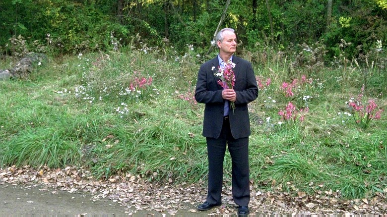 Don Johnston standing by the side of the road with a bouquet in Broken Flowers
