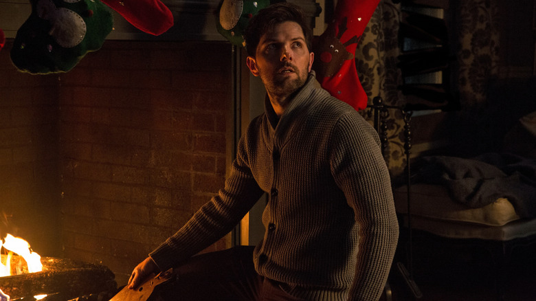 Tom, interpretado por Adam Scott, se asoma a la chimenea navideña y mira por encima del hombro a Krampus.