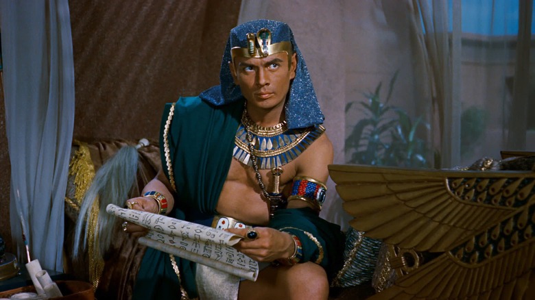 Ramesses II (Yul Brynner) stares off-screen with intensity while holding a large print papyrus in The Ten Commandments