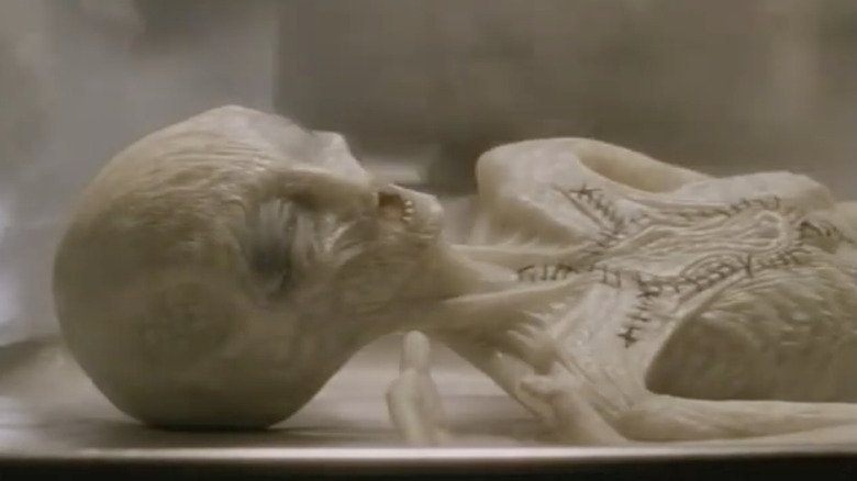 A dead gray alien rests on a slab in Dark Skies