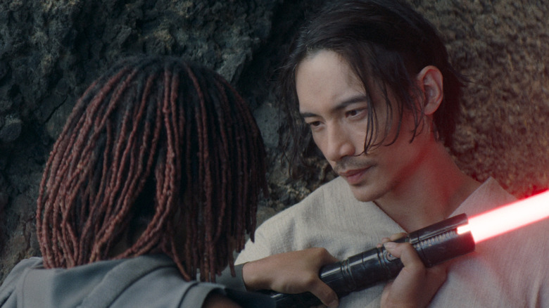 Qimir holding a stone-cold smolder, and his red lightsaber, as Osha attempts to attack him in Star Wars: The Acolyte