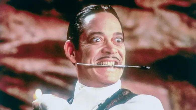 Gomez Addams holds a knife in his teeth
