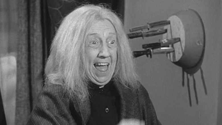 Grandmama Addams smiles in front of knife-board