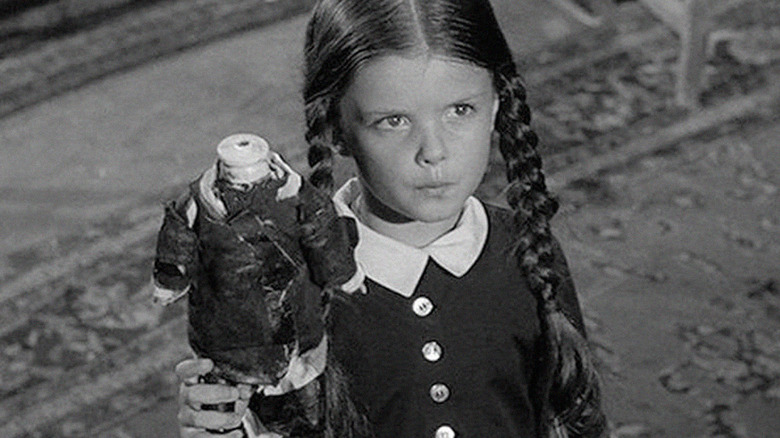 Wednesday Addams holds a headless doll