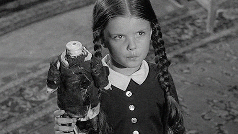 Wednesday Addams holds a headless doll